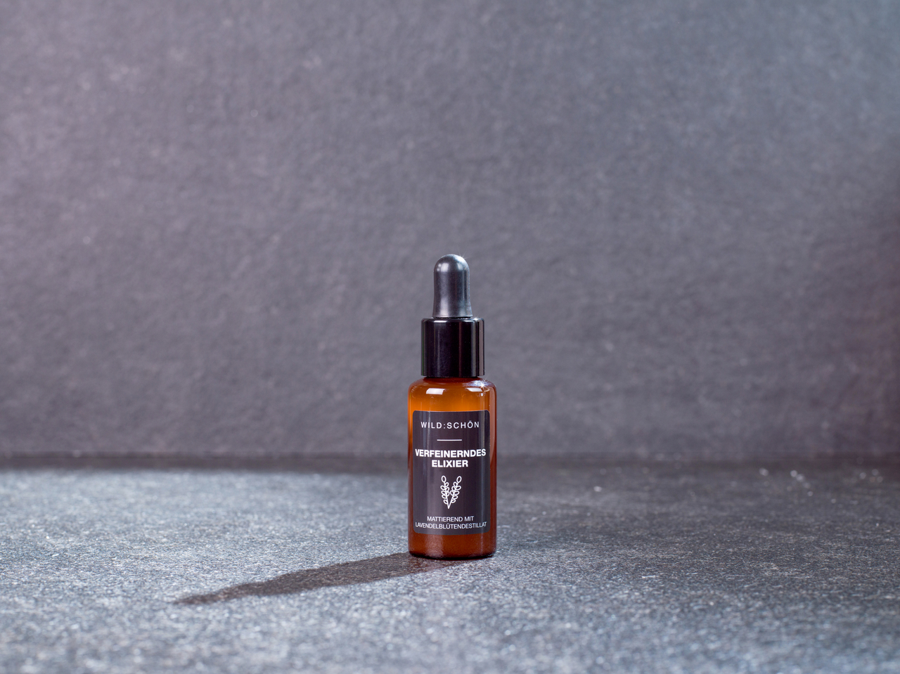 Wildschön Verfeinerndes Elixier Braunes Glasfläschchen mit Pipette, beschriftet mit 'WILDSCHÖN VERFEINERNDES ELIXIER', auf Hintergrund.