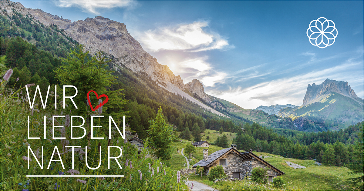 WIR ♥ LIEBEN NATUR Berglandschaft mit Wiesen, Wald und Hütten bei Sonnenuntergang. Text: ‚WIR ♥ LIEBEN NATUR‘.
